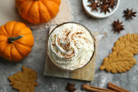Hot chocolate with whipped cream surrounded by pumpkins, cookies, and spices on a rustic surface