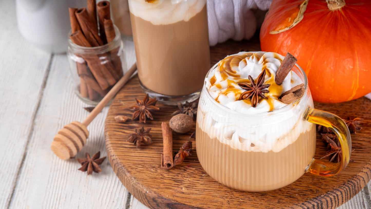 Pumpkin spice latte with whipped cream, cinnamon, and a honey dipper on a wooden coaster.